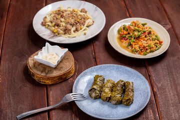 Couscous with vegetables, udon noodles with meat and homemade dolma on a wooden table