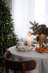 A beautifully warm and inviting Christmas holiday table decor with plates, candles, vase with spruces branches, teapot, mandarins.