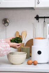 A beautifully stylish kitchen scene showcases a modern blender surrounded by vibrant fresh vegetables and eggs, woman hands with green leaves.