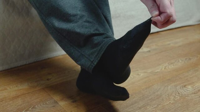 A man's feet in old black socks, one of which has a hole in the big toe