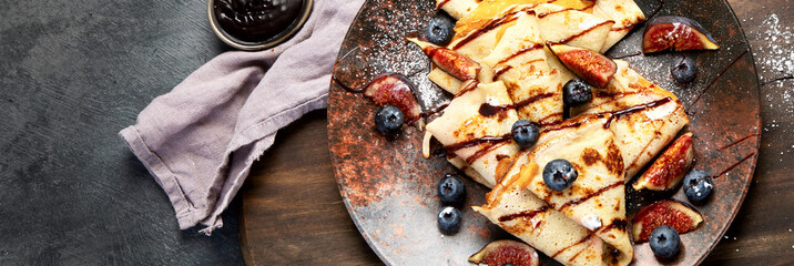Sweet crepes with figs and chocolate on gray background.