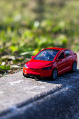 A bright red toy car is parked on the side of a busy road