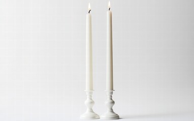 A set of two white taper candles in elegant holders, casting a cozy and festive glow on a clear white background