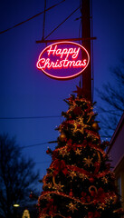 Christmas tree with ornaments, lit up at night. A pink neon sign that says "Happy Christmas" hangs above it