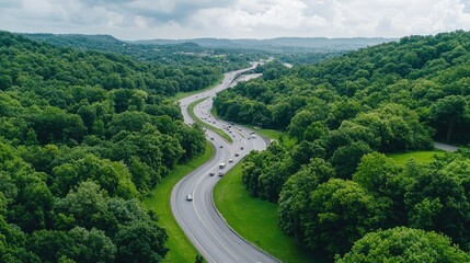 Fototapeta premium Winding highway curves through a dense green forest with cars driving on the road under an overcast sky.