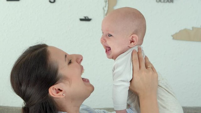
  Happy woman is enjoying motherhood with her newborn baby son at home. Lifting  baby up,  baby laughs merrily. 