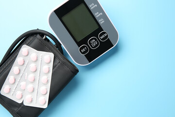 Blood pressure measuring device and pills on light blue background, top view. Space for text