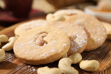 Tasty cashew cookies with powdered sugar on wooden board, closeup