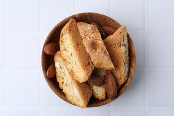 Tasty almond biscuits (Cantuccini) and nuts in bowl on white tiled table, top view