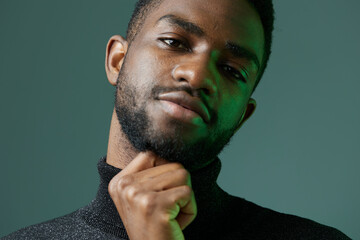 Thoughtful african american man in stylish turtleneck sweater contemplating with hand on chin,...