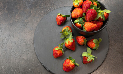 Fresh ripe organic strawberry in a black bowl on a dark slate, stone or concrete background. Top view with copy space.