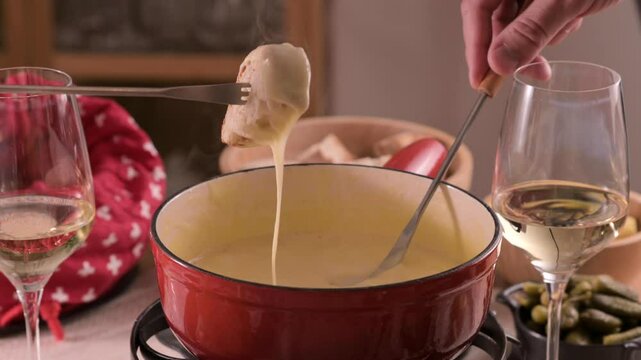 Cozy Swiss fondue setup with melted cheese, bread, pickles, and wine on a rustic table. advertising, social media campaigns, or food-related promotions. High quality 4k footage