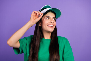 Naklejka premium Smiling young woman wearing green t-shirt with visor cap on vibrant purple background capturing joyful and playful emotions