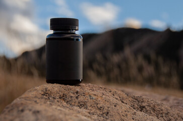 Minimalist black bottle with blank label in mountain nature rock background for wellness concept