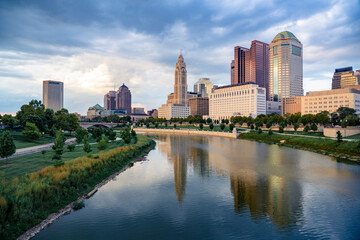 Scenic view of downtown Columbus, Ohio, during a calm evening with soft lighting, the skyline with modern skyscrapers and historic buildings reflecting in the Scioto River in the foreground