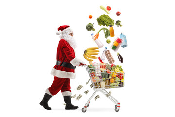 Full length profile shot of Santa Claus walking and pushing a shopping cart with falling groceries and money