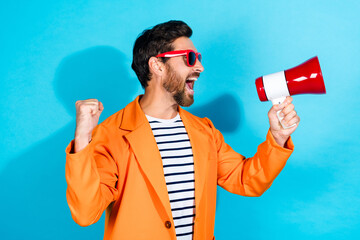 Energetic young man in a bright orange jacket enthusiastically shouting into a red megaphone...
