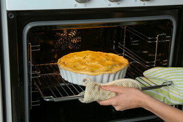 Woman putting homemade apple pie into oven in kitchen, closeup