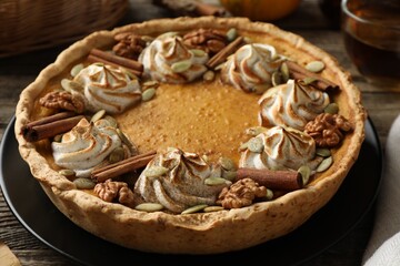 Homemade pumpkin pie with whipped cream, seeds and cinnamon on wooden table, closeup