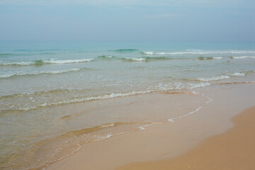 A peaceful beach scene showing gentle ocean waves lapping onto the sandy shoreline under a soft blue sky.

