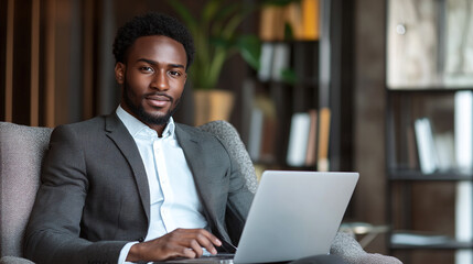 Handsome young african american man sitting on the chair in the room at a house or home, and using a laptop or notebook. male adult freelancing, working online on the internet.