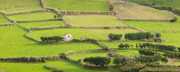 Rural landscape in panorama format with green fields, stone walls and small stone barns on the isle of Flores, Azores Portugal