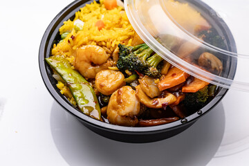 Close-up of a plastic bowl with a lid, filled with Chinese takeout fried rice, shrimp, and vegetables in garlic sauce.