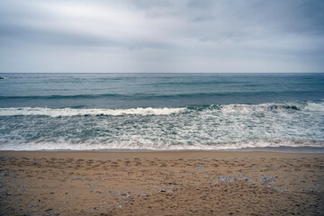 Beach scene with sandy shore and ocean in the background. Cloudy sky and soft waves highlight the natural beauty of the coastline and sea