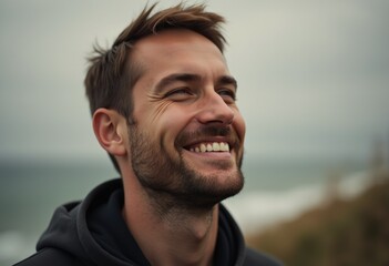 Fototapeta premium A joyful man with a beard, laughing and looking up at the sky, outdoors near the ocean.