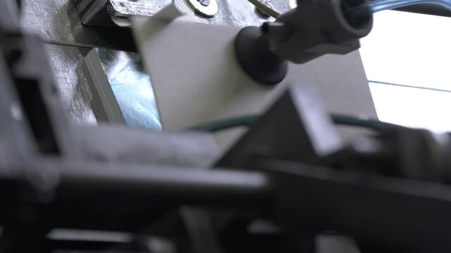 Suction cup takes and moves cut cardboard sheets using machine in workshop. Material loses integral structure for further production of finished product
