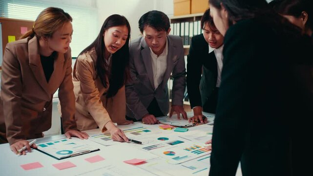 Professional businesspeople analyzing graphs, charts, and reports while collaborating closely in modern, bright office environment, showcasing strategic teamwork and data-driven innovation