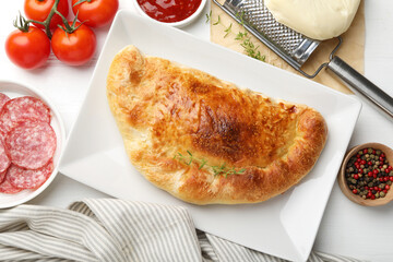 Delicious fresh calzone pizza and ingredients on white table, flat lay