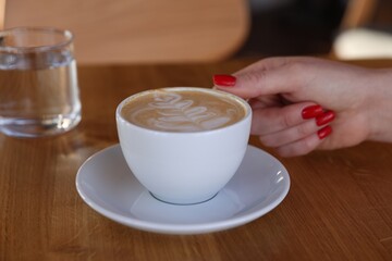 Woman with cup of aromatic coffee at wooden table in cafe, closeup