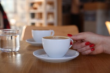 Woman with cup of aromatic coffee at wooden table in cafe, closeup