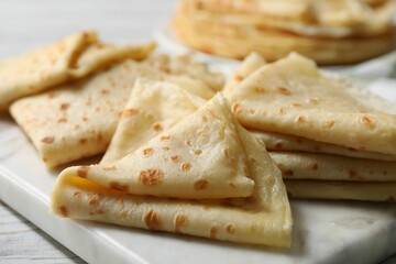Many tasty crepes on white wooden table, closeup