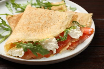 Delicious crepes with salmon, cream cheese and arugula on wooden table, closeup