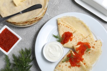 Tasty crepes with red caviar, dill and sauce served on grey textured table, flat lay