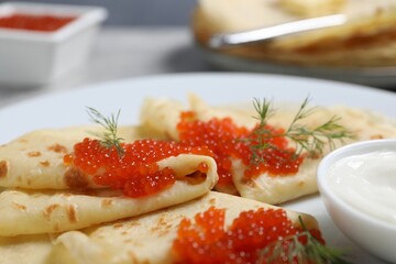 Tasty crepes with red caviar, dill and sauce on grey table, closeup