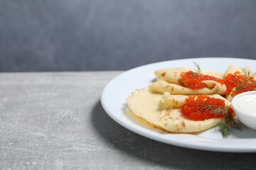 Tasty crepes with red caviar, dill and sauce on grey textured table, closeup. Space for text