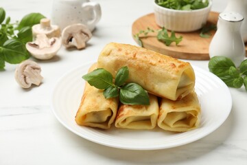 Delicious rolled crepes with basil and mushrooms on white marble table, closeup