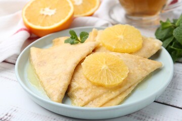 Delicious Crepes Suzette, mint, tea and oranges on white wooden table, closeup