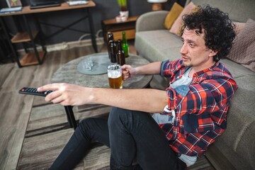 Young man drinking beer and watching tv at home