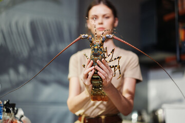 Female chef holding a live lobster in modern kitchen setting