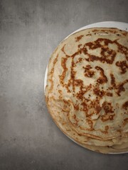 Stack of homemade crepes resting on a white plate on a gray surface copy space
