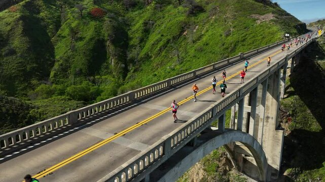 Big Sur marathon race as runners cross famous Rocky Creek bridge.  Waving to the camera.