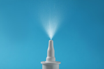Nasal spray with sprinkled medication over nozzle on light blue background, closeup