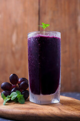 a glass of black grape juice on a wooden background.