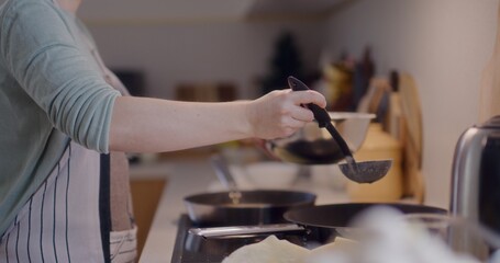 Woman Scooping Pancake Batter with Ladle in Kitchen While Cooking