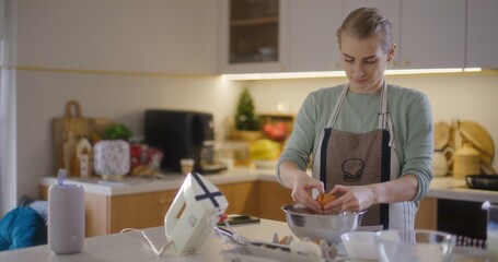 Woman cracks raw egg into bowl of flour and prepares dough for baking