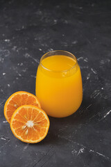 glass of orange juice on an old wooden table, with a patterned black background